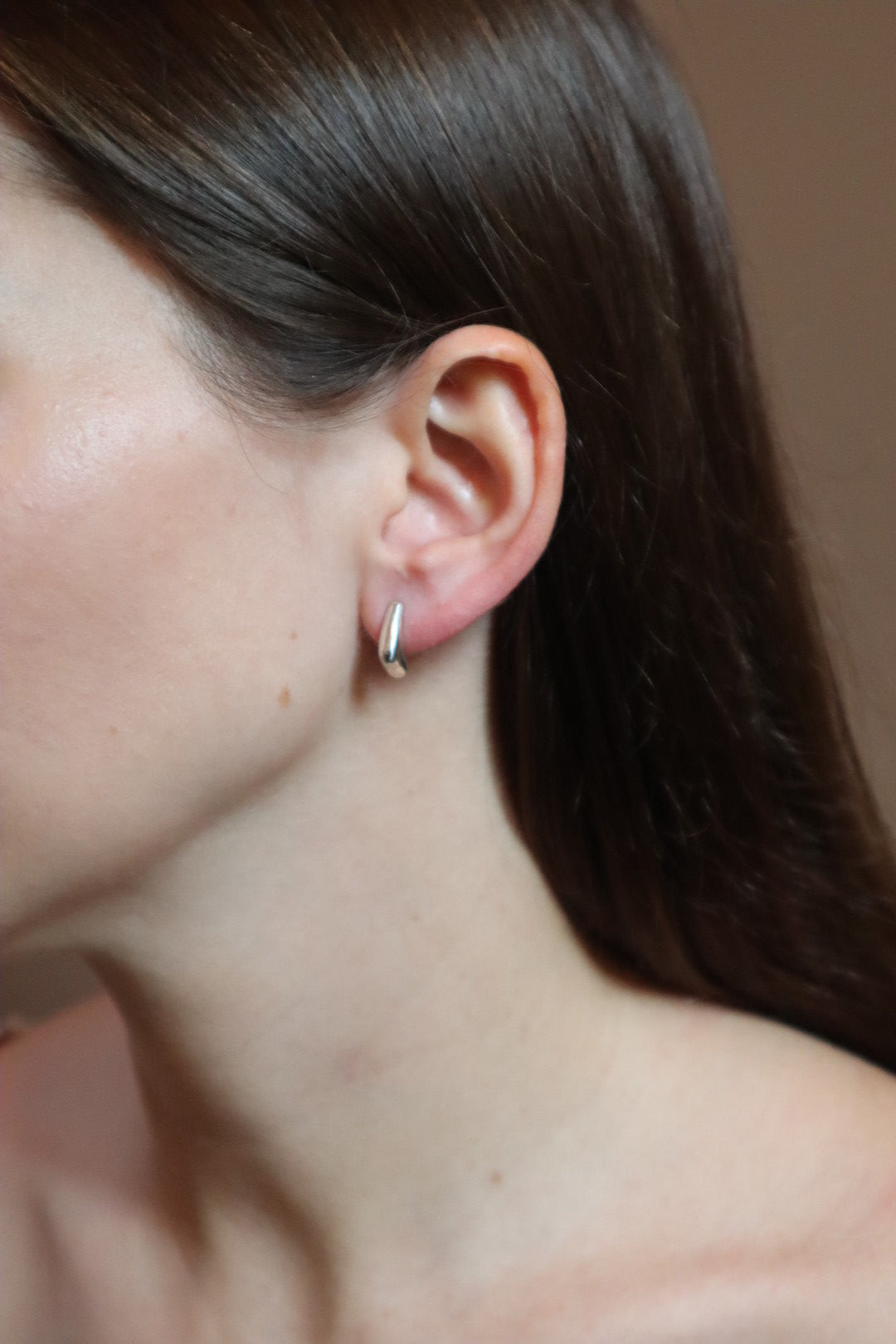 Close-up of an ear with a small earring against a neutral background